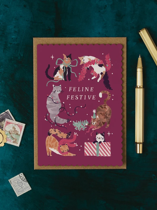 Feline Festive Cats Christmas Card by Sister Paper Co on a kraft envelope with a gold pen, on a dark teal background