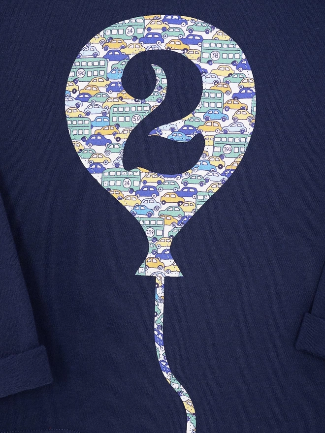 A navy cotton long sleeve t-shirt. The t-shirt features a balloon with the number 2 cut out from it, appliquéd in a cars Liberty print. 