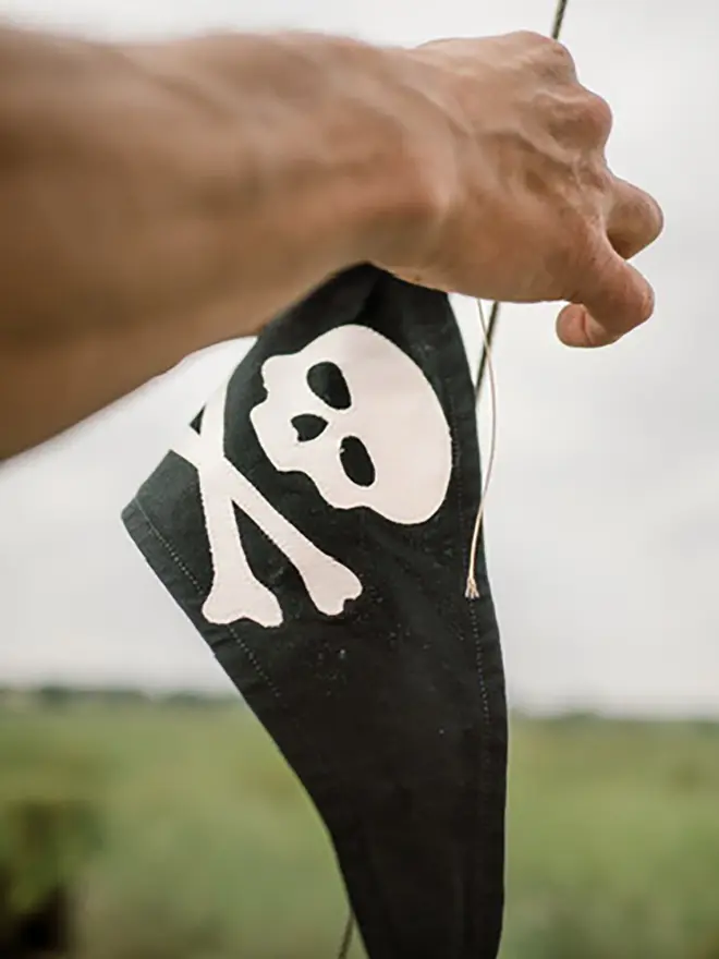 somebody tying a black pennant flag with an ivory skull and crossbones onto a boat mast