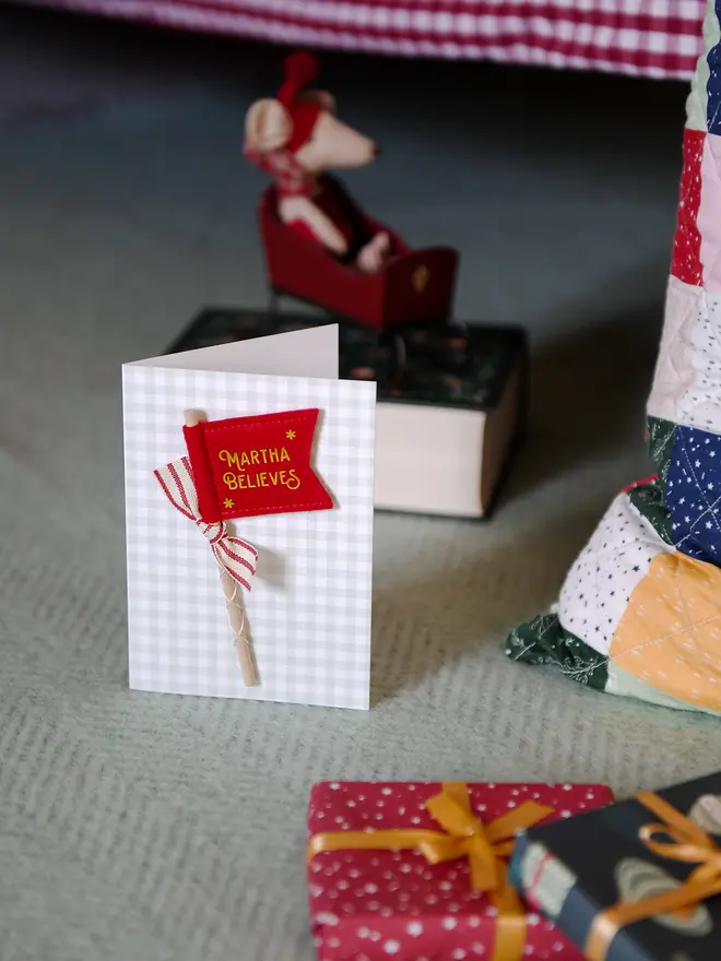 A Christmas card with a tiny handmade felt flag attached. The flag reads 'Martha Believes' and has a red striped ribbon tied to it.