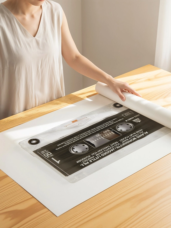 jagged little pill alanis morrisette cassette tape print. print being unrolled on wooden table.