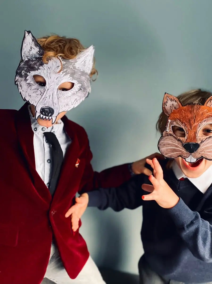 Cut And Create Forest Animals Children’s Masks, two young children posing playfully while wearing homemade paper animal masks of a grey wolf and an orange squirrel.