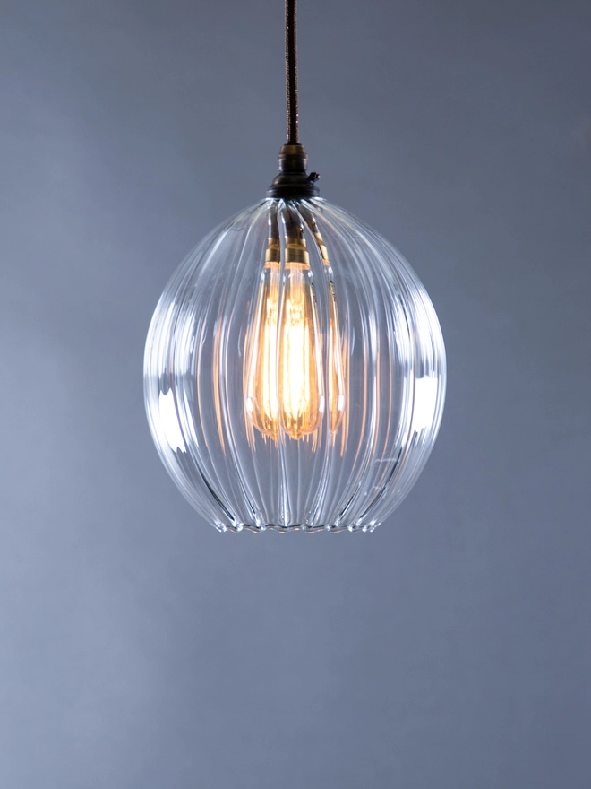 Small Clear ribbed Wanda Globe Pendant Light with the light on. 