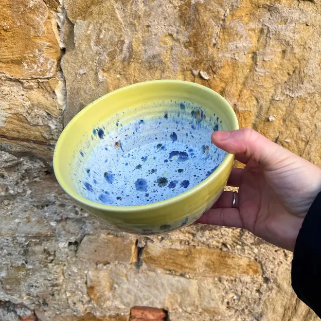 Shoreline Ramen Bowl, a person holding a colourful ramen bowl against a brick backdrop. 