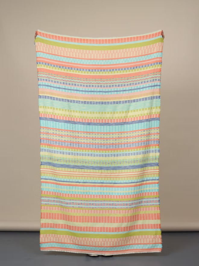 indie lambswool blanket. a multicoloured blanket photographed against a plain wall.