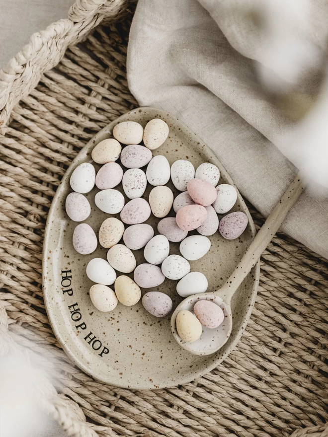 ceramic egg shaped plate filled with mini eggs, with the words 'hop hop hop' around the edge