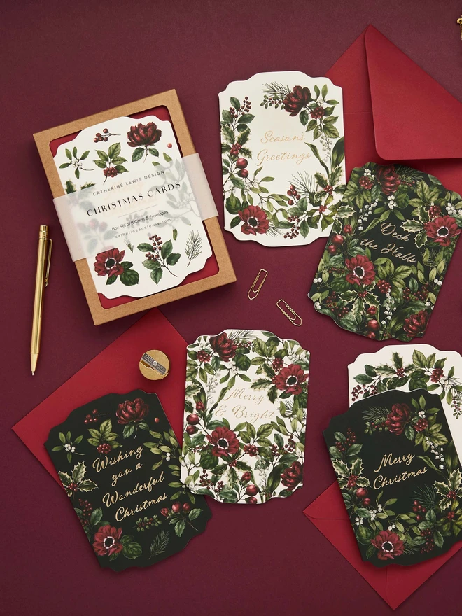 Box of 8 cards, with red envelopes. gold foil and die-cut shape cards with greens and red botanicals