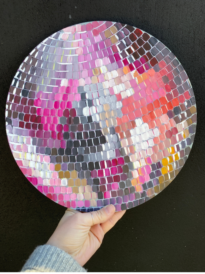 a hand holding a colourful round disco ball painting