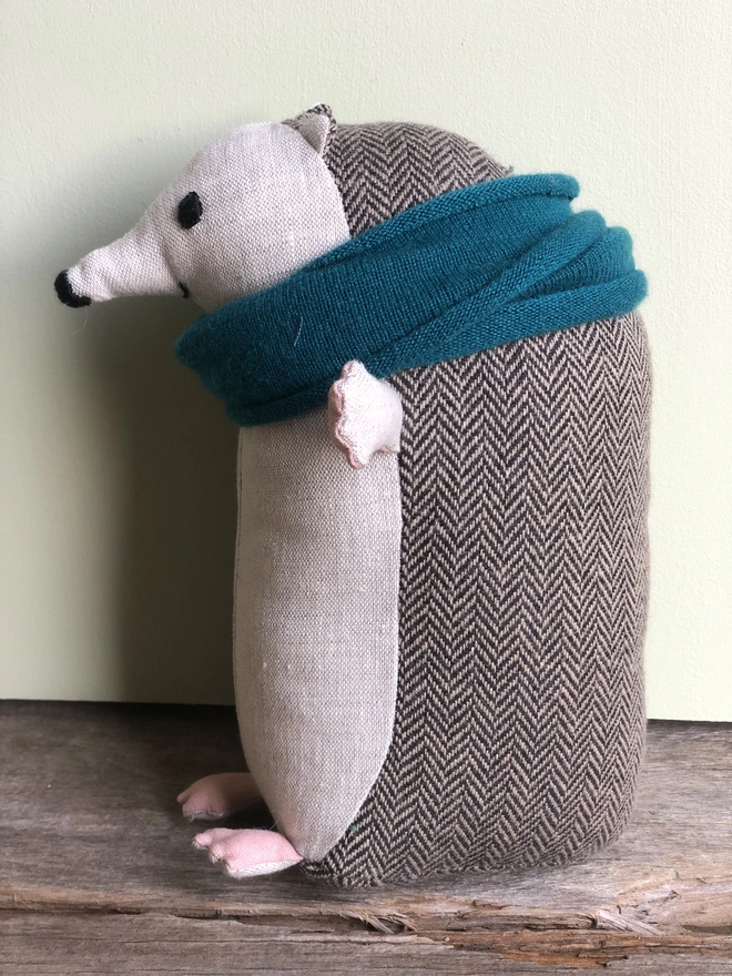 Handmade fabric toy hedgehog, made from natural linen (front) and brown herringbone tweed (back), wearing a blue lambs wool scarf, with embroidered eyes,nose and mouth