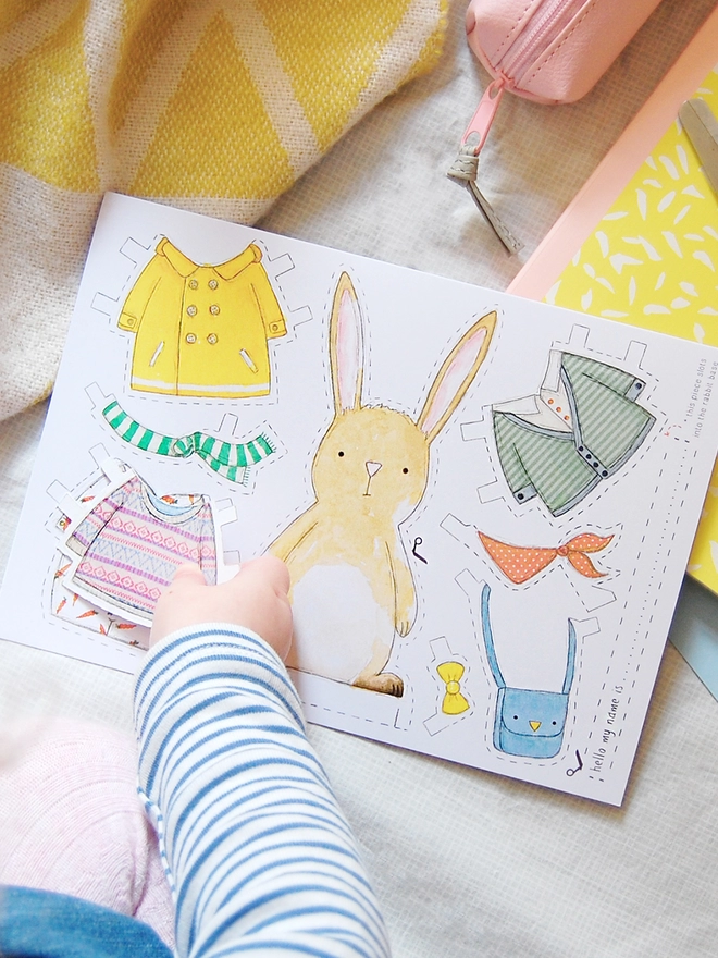 A child is playing with a dress up rabbit paper doll that has been cut from an illustrated greetings card.