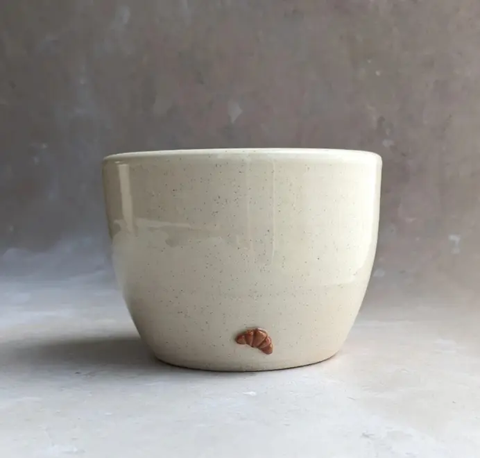 Vanilla bean–colored croissant coffee cup with a subtle croissant design, placed against a grey marble background.