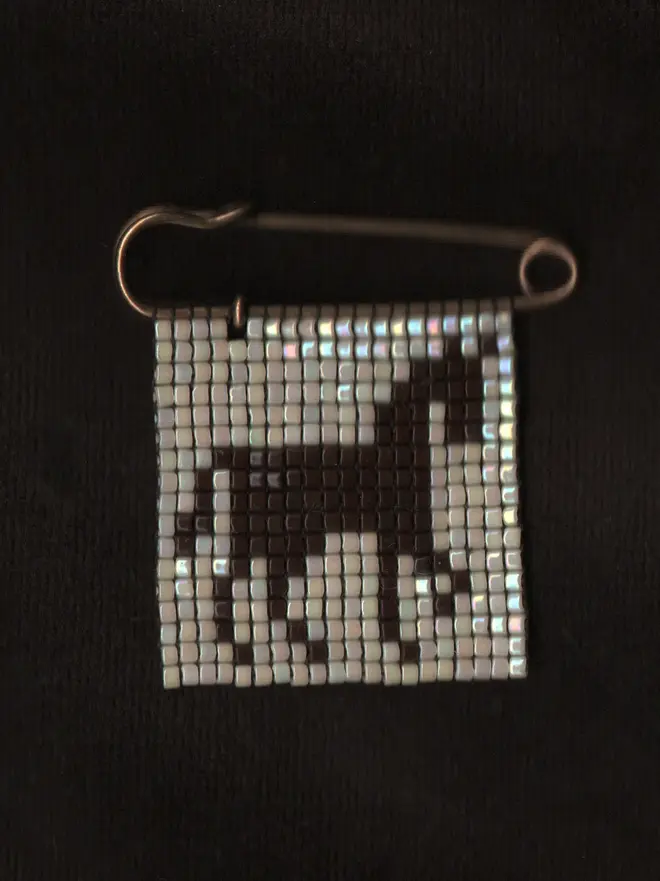 'creature viii' beaded pin. a beaded pin badge with a brown horse silhouette on a pearl background.