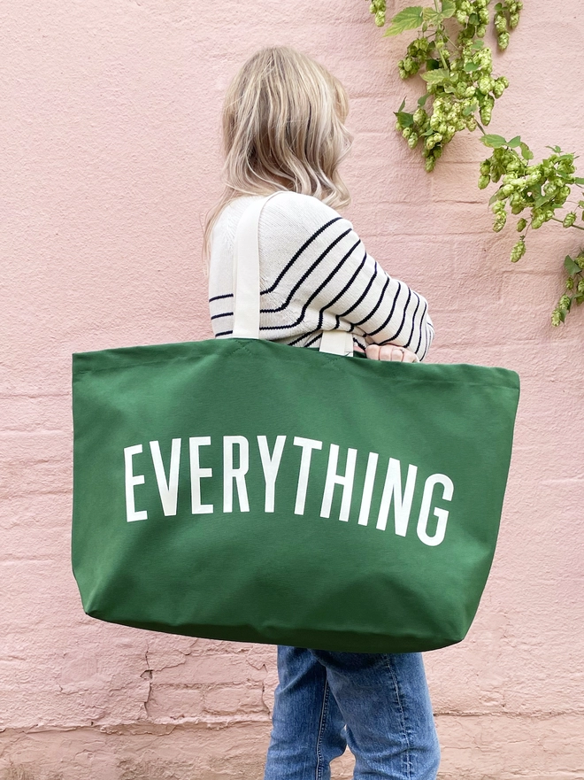 Model carrying the Everything oversized tote bag in green canvas in front of a pink wall