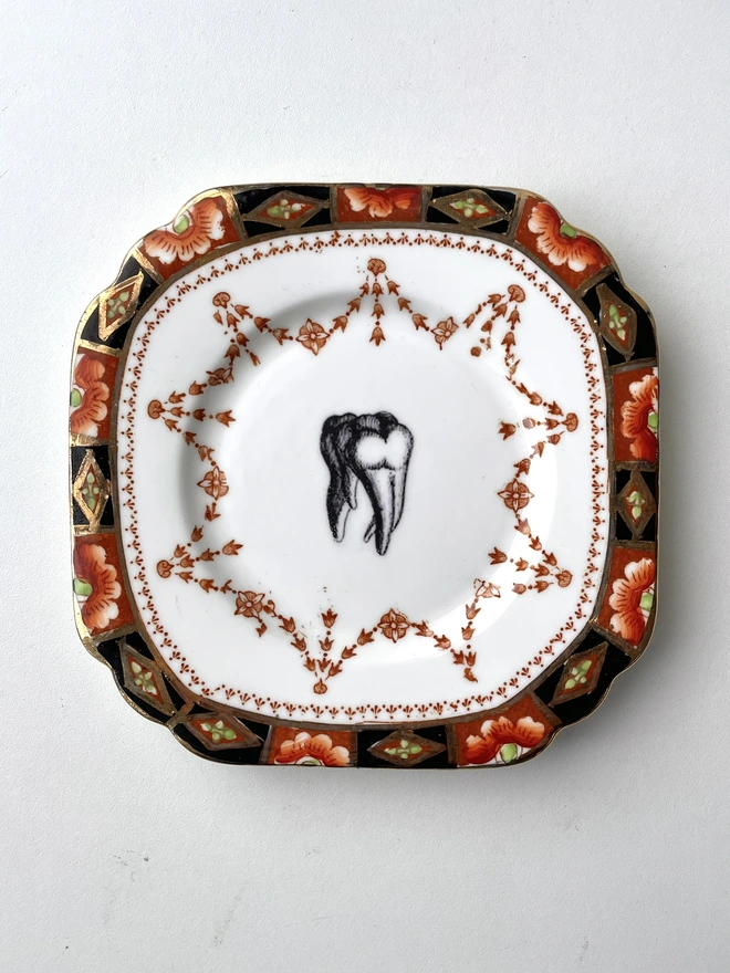 vintage plate with ornate border has a black and white image of a victorian molar tooth in the centre