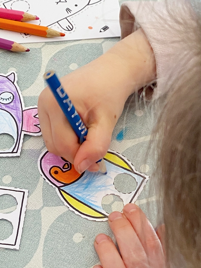 A child is colouring in several card finger puppets.