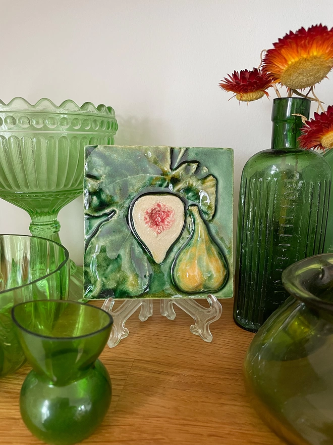 Decorative eye-catching fig feature tile – three-dimensional, very realistic and incredibly tactile - displayed on a mantelpiece alongside antique green glass. 