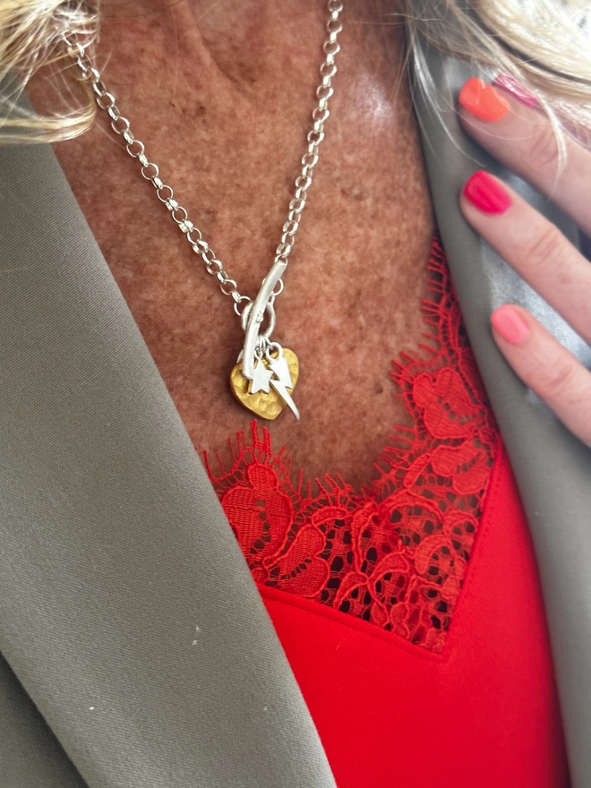 model wears silver t bar chain with large textured heart charm in gold, with a mini star and lightning bolt in silver