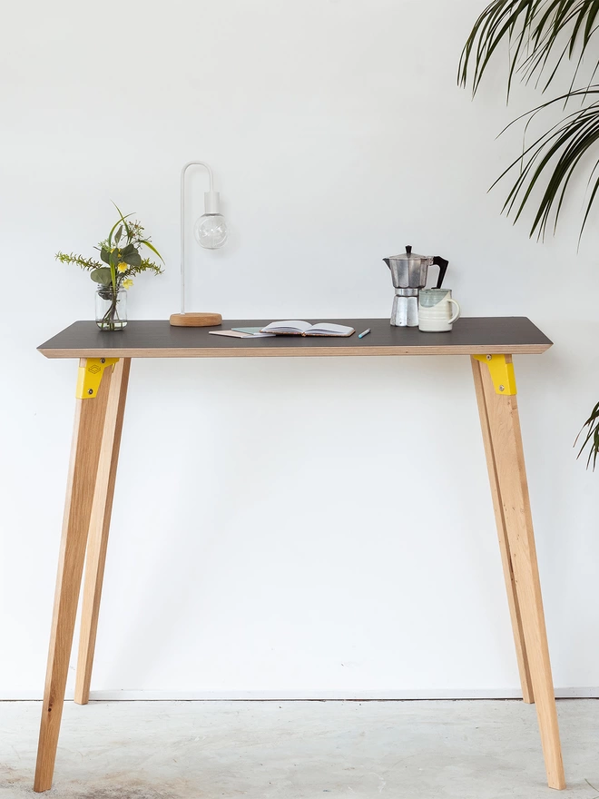 A stylish and minimalist standing height desk with charcoal Fenix top, yellow coloured steel brackets and solid oak legs.