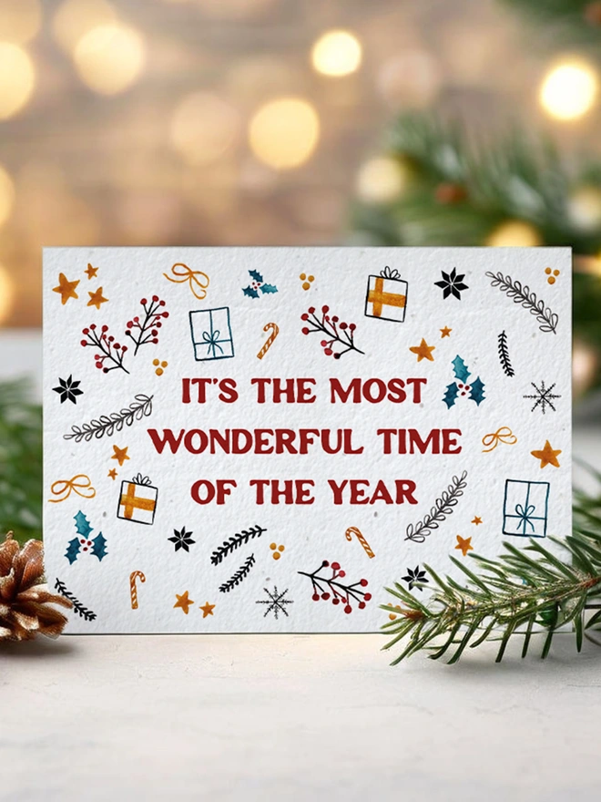 Christmas card with twinkly lights, greenery and pine cones. The Christmas Card features Christmas illustrations with 'Its the most wonderful time of the year' on