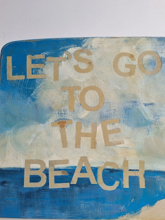 Upcycled art panel in blues and creams featuring a seascape and an image of a retro pin-up lady on a boat and the text reads ‘let’s go to the beach’ in a distressed, shabby chic style