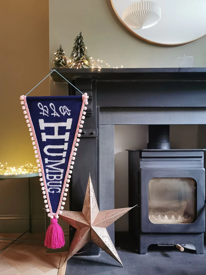 A Bah Humbug pennany flag hangs from a black fireplace surround. A copper paper star and some subtle copper wire lights create a cosy Christmas glow.