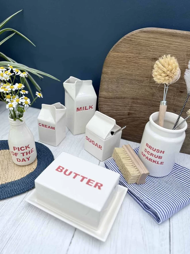 A handmade ceramic butter dish stands with matching flower bottle, sugar pot, milk and cream carton.