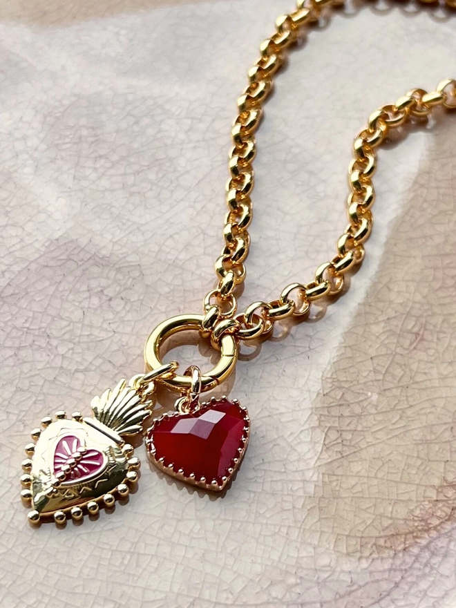 Chunky gold charm necklace on pink ceramic plate with two red heart charms