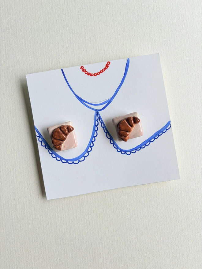 Foodie collar pins. Small square collar pins with a tiny croissant attached on a collar hand-sketched on paper 