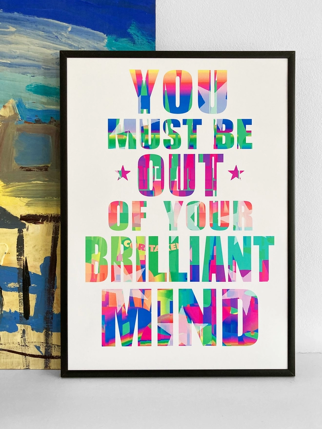 Framed multicoloured typographic poster with song lyric by the band, Furniture - "You must be out of your brilliant mind”. The print rests against a blue and yellow abstract painting.