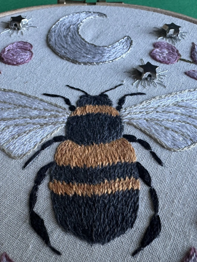 A close up of an embroidered bee with a silver crescent moon 