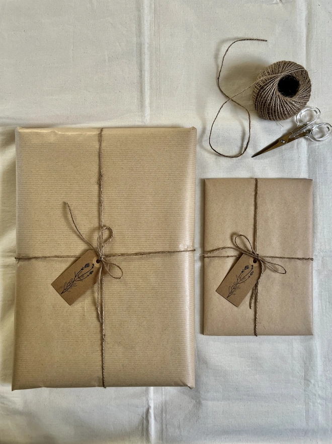 two different size artworks gift wrapped in brown paper with a hand stamped flower tag and brown string 