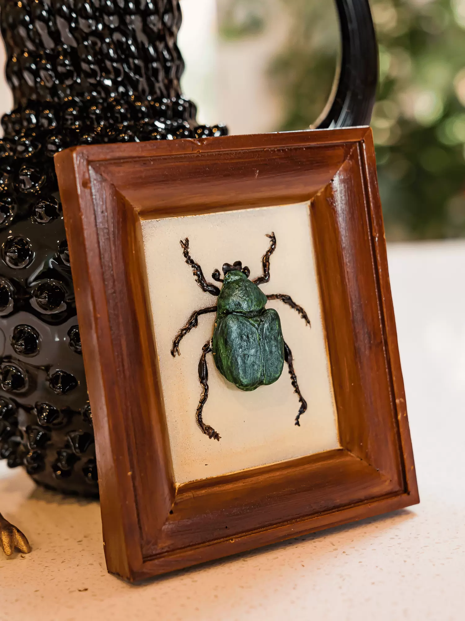 Realistic edible chocolate Chafer beetle in chocolate frame propped against an antique jug on a table