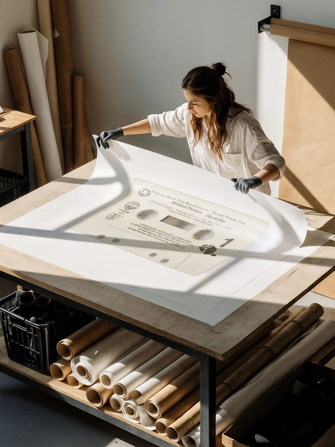prince purple rain cassette tape print. artist unrolling print on studio desk