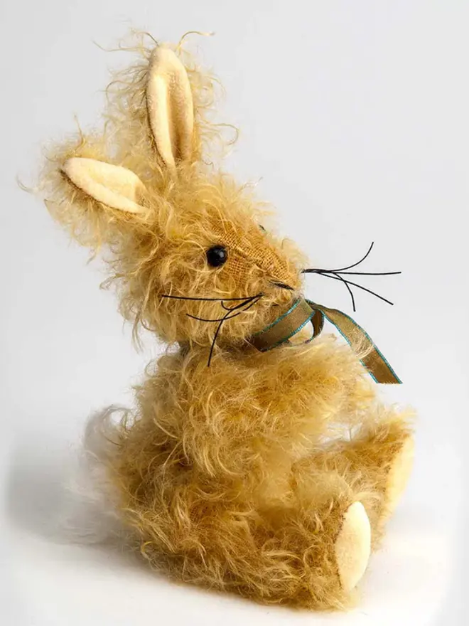 Brown stuffed rabbit sitting upright against a white background, wearing a green and blue ribbon.