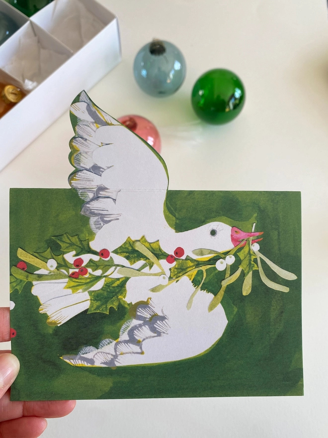 Esther Kent illustrated Christmas Card showing white goose on green inky background, carrying holly and mistletoe