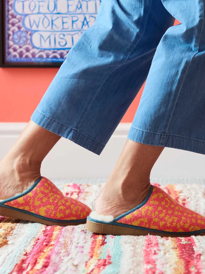 Lambswool & Sheepskin Slippers, a pair of colourful lambswool and sheepskin slippers sitting modelled in front of a colourful wall. 