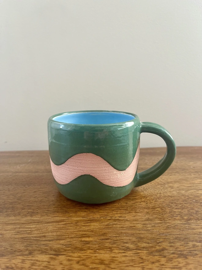 Hand-thrown ceramic flat white mug with forest green glaze, exposed clay wave design, bright blue interior and chunky ribbed handle, handmade by Hannah Inskip Pottery.