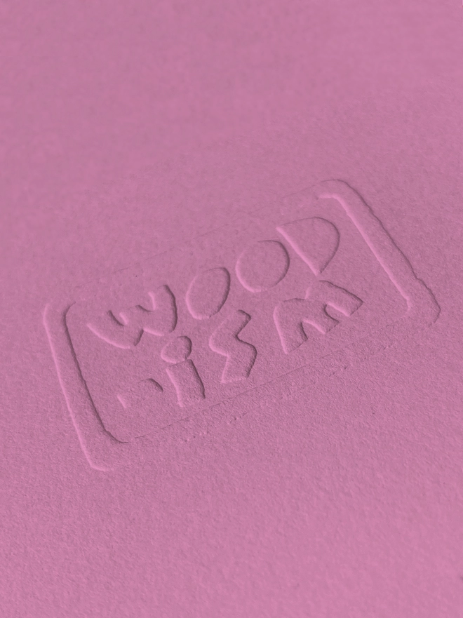 A close up of a pink Woodism print with an embossed Woodism logo 