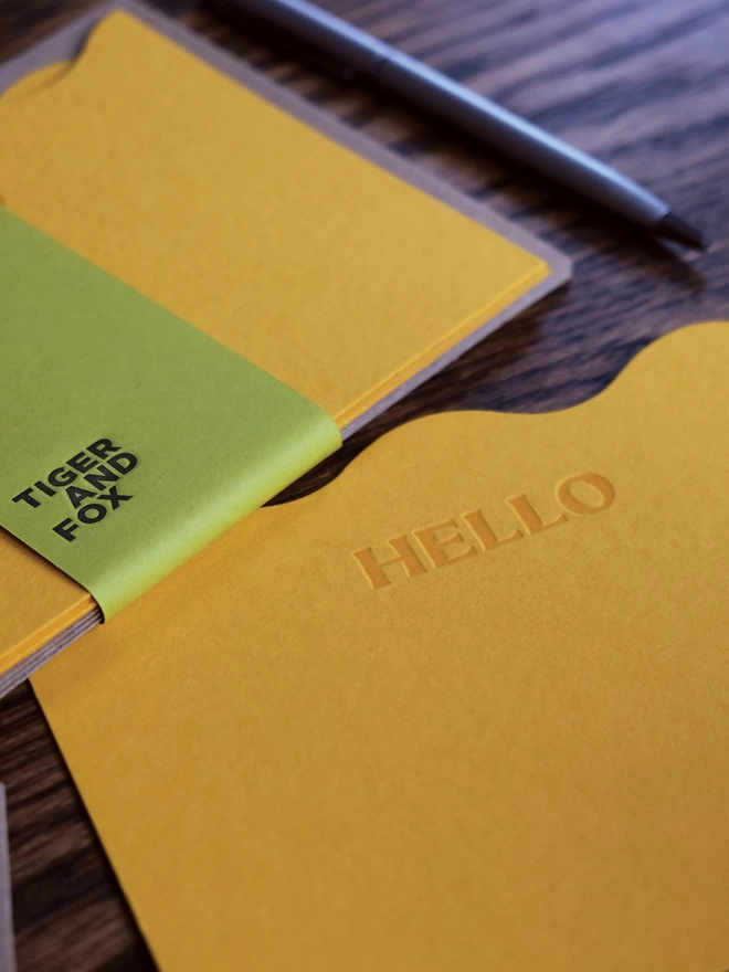 Wavy 'Hello' notecard set with green paper bellyband and pen.