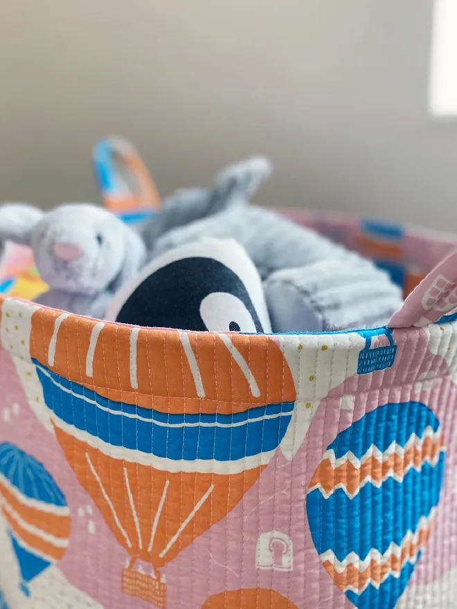 Close up of Balloons at Dawn Quilted Storage Basket filled with soft toys.