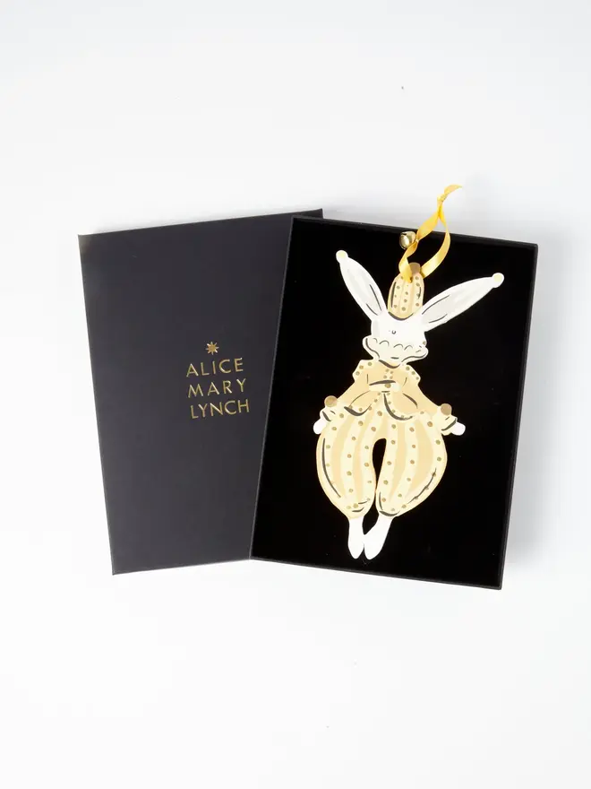 Hare Tree Dancer. wooden hanging hare decoration in an open black gift box embossed "alice mary lynch" in gold, with a gold top hat, cream polka dot pantaloons with a bow and gold ribbon with a jingle bell
