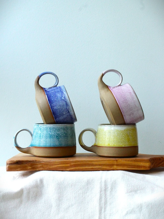 Four handmade ceramic cups with pastel glazes—blue, yellow, teal, and pink—