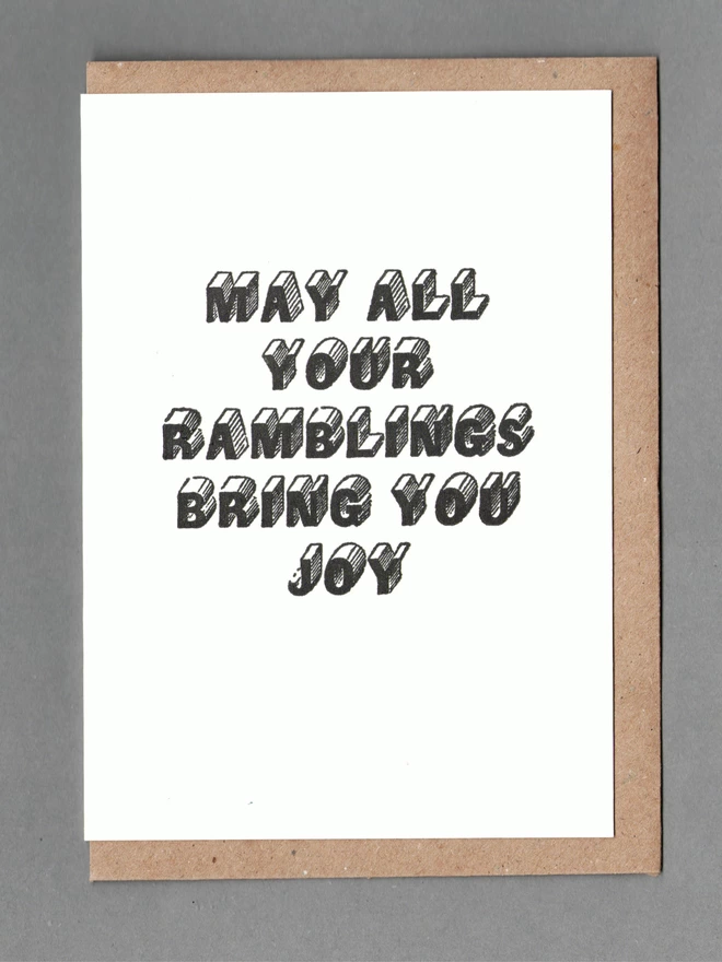 White card with black text reading 'MAY ALL YOUR RAMBLINGS BRING YOU JOY' with a kraft envelope behind it