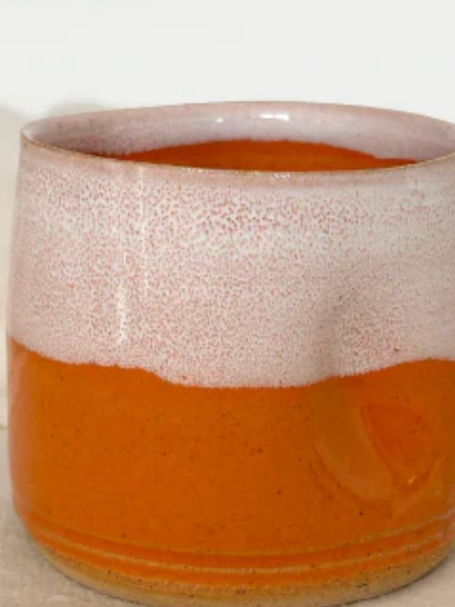 Pinch Mug. Close up of an Orange Mini Pinch Mug against a cream background.