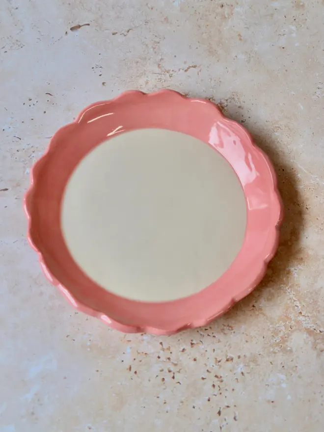 Handmade ceramic plate with pink scalloped rim — full view from above