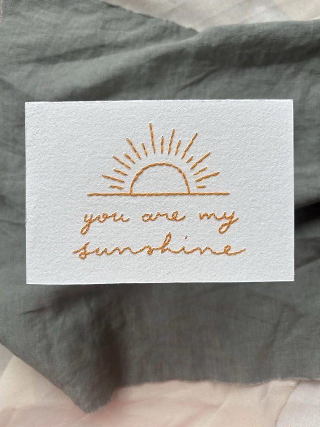 You are my sunshine hand embroidered card with yellow cursive lettering on a white background 