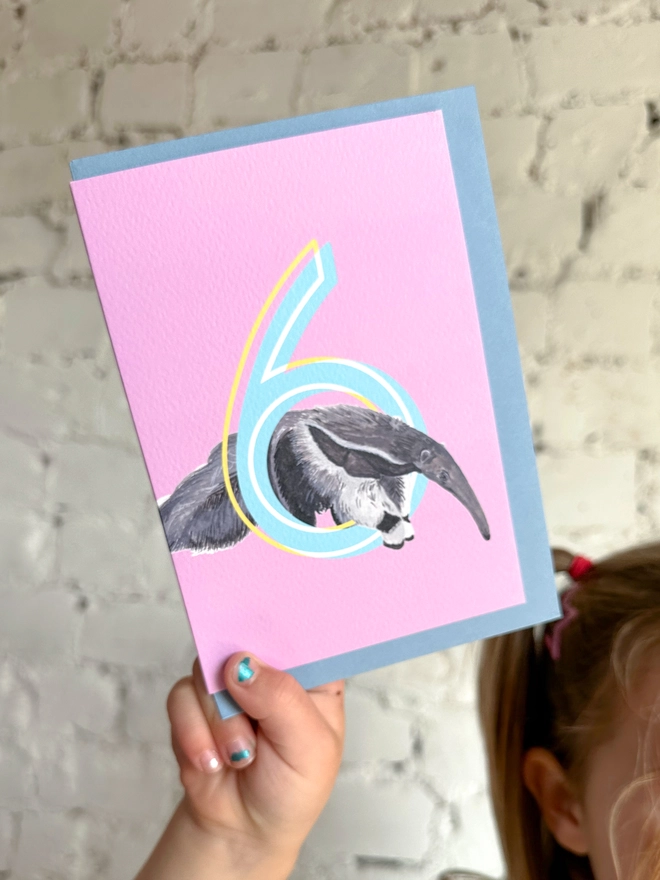 a pink card featuring a big blue number 6 and a giant anteater illustration with a blue envelope