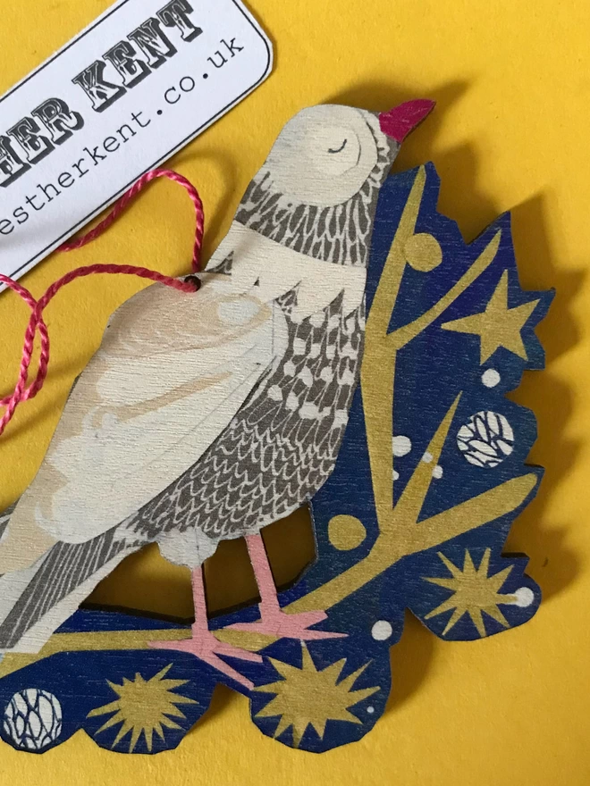 Illustrated peace dove standing on a gold star-spangled twig on a blue backround. The cut-out decoration rests on a yellow background.