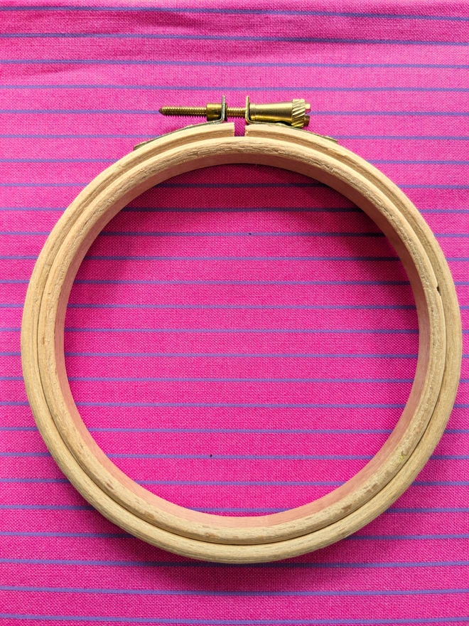 A wooden embroidery hoop lying on a stripy pink fabric