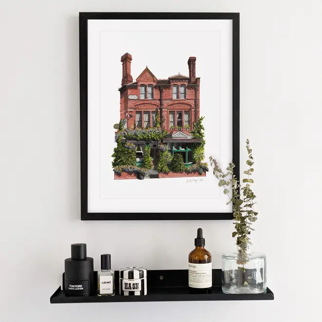 Nunhead Skehans Giclée Print (Unframed), a print of a brick pub in a black frame against a plain backdrop in a bathroom. 